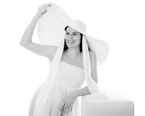 Schwangere Frau in weißem Kleid und Hut vor weißem Hintergrund