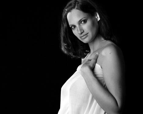 Schwangere Frau in Seitenansicht mit weißem Tuch im den Körper vor schwarzem Hintergrund