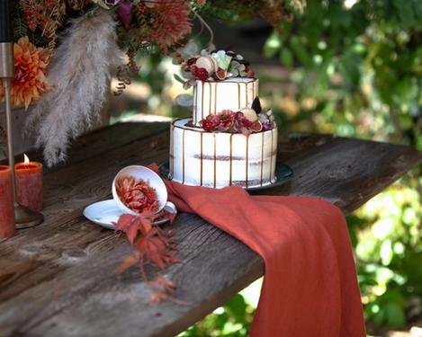 Zweistöckige Hochzeitstorte mit rostfarbiger Deko wie Tuch, Blumen und Kerzen