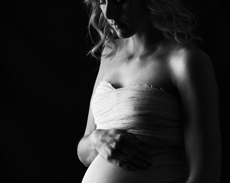 Schwangere Frau im Seitenlicht vor schwarzem Hintergrund