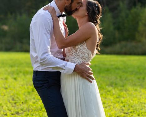 Bride and groom kiss each other on the green meadow with backlight
