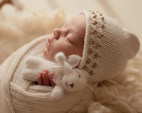 Kopf eines Neugeborenen mit weißer Mütze und Teddy in Profilansicht