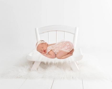Newborn baby sleeping in white lace bodysuit on white armchair