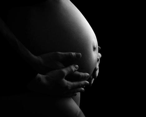 Seitenansicht eines nackten Babybauchs umarmt von ihren und seien Händen; Schwarzer Hintergrund, sw-Bild
