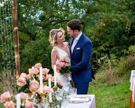 Weiße und rosa Hochzeitstorte auf einem goldenen Tablett, im Hintergrund der rosa gedeckte Hochzeitstisch