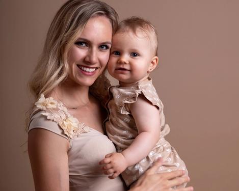 Portrait of a mother with her one-year-old baby smiling at the camera. Both are dressed in beige in a studio set of the same colour.