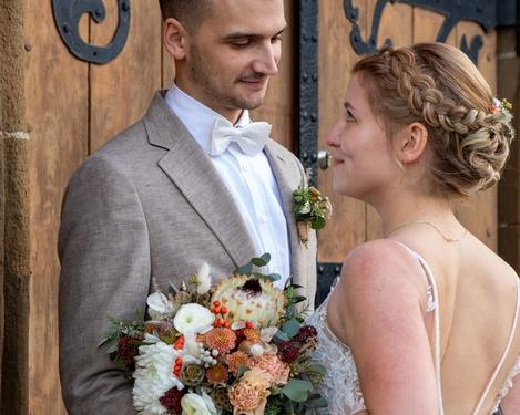 Bride and groom stand in front of an old wooden portal and look at each other with a smile