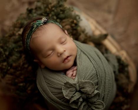 Baby mit Stirnband eingewickelt in oliv grünem Tuch auf dunklem Holzboden