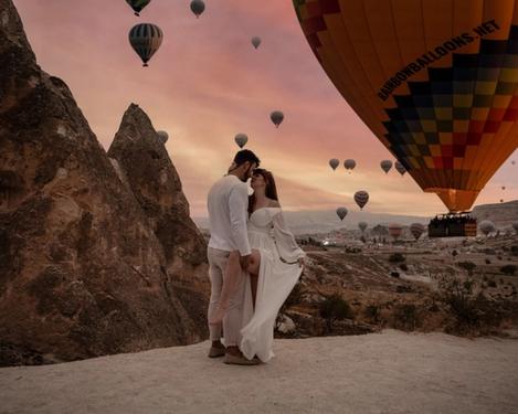 Couple in love in the mountains at sunrise with many hot air balloons in the background