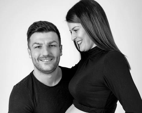 Pregnant woman in jeans and black top stands close to her partner b&w shoot