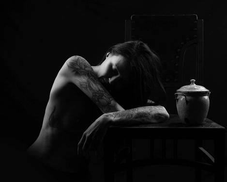 Upper body of a woman with tattoos on her arms, leaning over a table, b/w picture