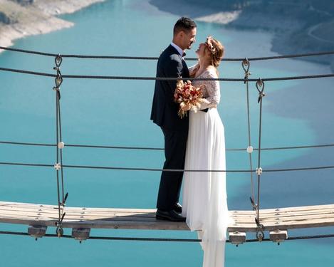 Bride and groom are facing each other on a suspension bridge, in the background you can see a lake