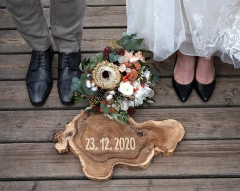 Brautstrauß, Holzplatte mit Hochzeitsdatum umrahmt von den Füßen des Hochzeitspaares