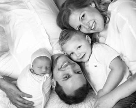Family with newborn and toddler lie on white fur and smile to camera