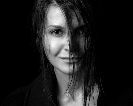 Portrait einer dunkelhaarige Frau, mit Haarsträhnen zum Gesicht, dunkler Hintergrund