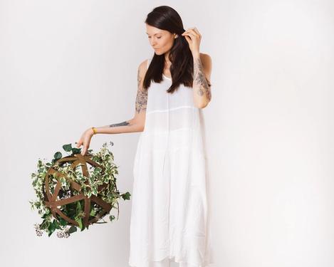  Woman dressed in white holds a ball covered with ivy, studio shot