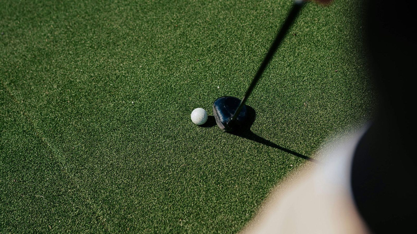 A close-up of a golfer preparing to hit a golf ball with a club on a green, well-maintained grass surface. Perfect for illustrating golf lessons or showcasing the vibrant golfing scene in Golf London. The image highlights the ball and club in sharp detail.