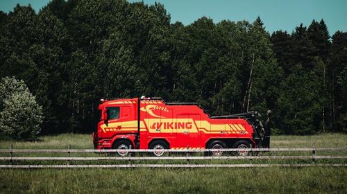 Punainen hinausauto, jonka kyljessä on teksti "Viking", on pysäköity nurmikentällä, puuaidan ja taustalla metsäpuiden ympäröimänä.