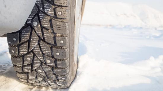 Lähikuva auton nastarenkaasta lumisella tiellä.