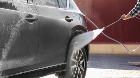 A person is washing the back of a black car with a pressure washer.