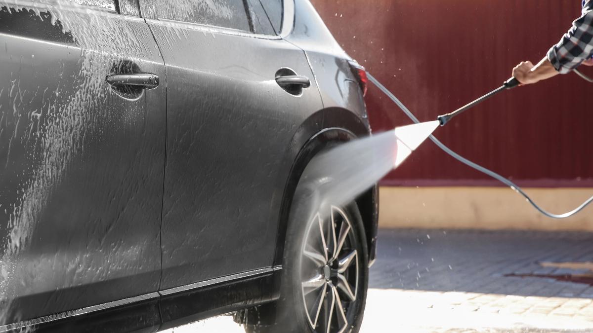Person som vasker bilen utvendig med høytrykk.