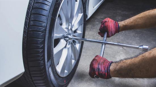Henkilö kiristää ristikkoavaimella autonrenkaan pultteja.