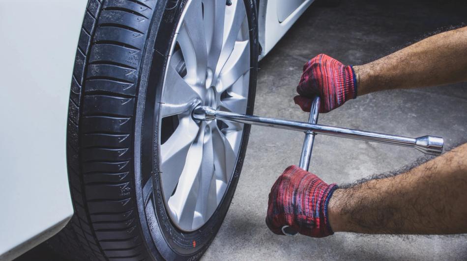 Henkilö kiristää ristikkoavaimella autonrenkaan pultteja.