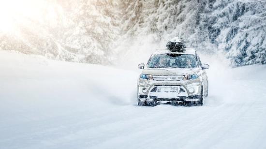 Katumaasturi, jonka katolla on suksiboksi, ajaa talvella lumisella metsäisellä tiellä.