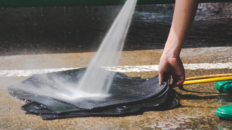 Henkilö puhdistaa painepesurilla mustat auton kumimatot.