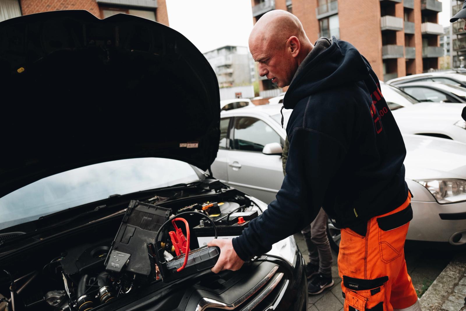 Mies käynnistää autoa parkkipaikalla apuvirtalaitteella.