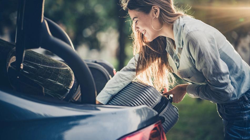 Nainen laittaa matkalaukkua auton takakonttiin ulkona.