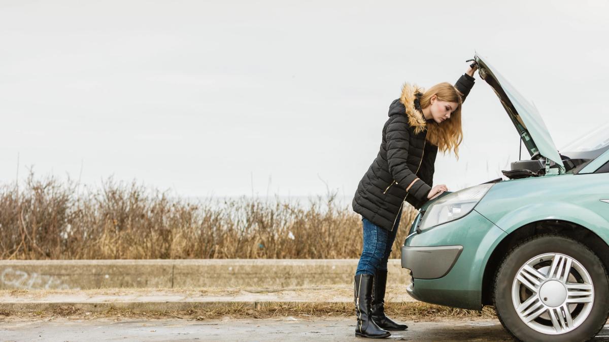 Nainen seisoo auton keulan edessä ja katsoo moottoria tiellä.