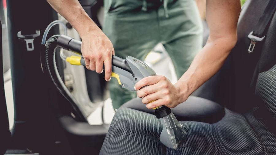 Henkilö puhdistaa auton kangasistuimia tekstiilipesurilla.
