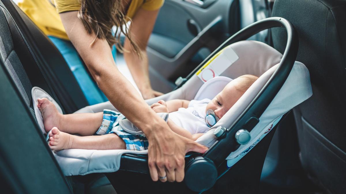 Kvinne plasserer barn i barnesete i bil.