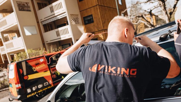 Viking T-paitaan pukeutunut henkilö käyttää työkaluja auton oven lukituksen avaamiseen.