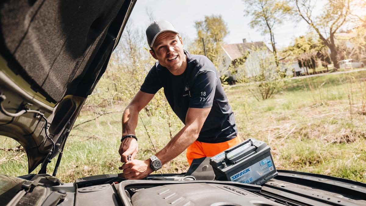Mann som bytter bilbatteri på bilen selv.