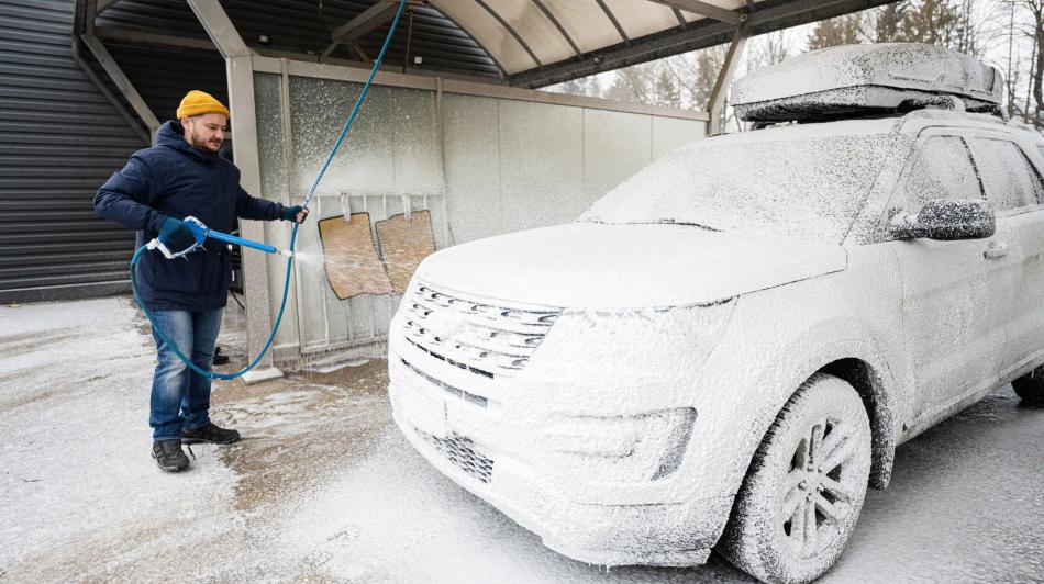 Mies, jolla on keltainen pipo, pesee vaahdon peitossa olevaa maastoautoa autopesuaseman katoksen alla.
