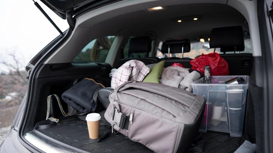 Auton avonainen takakontti täynnä laukkuja, vaatteita, astioita ja take away -kahvikuppi.