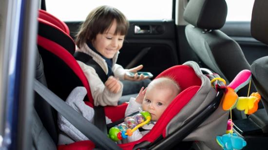 Pieni lapsi hymyilee auton takapenkillä kasvot menosuuntaan asennetussa turvaistuimessa vierellään vauva, joka on selkä menosuuntaan asennetussa turvakaukalossa.