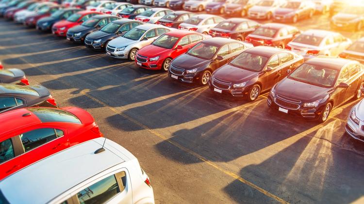 Parkkipaikalle pysäköityjä erilaisia autoja kirkkaassa auringonvalossa.