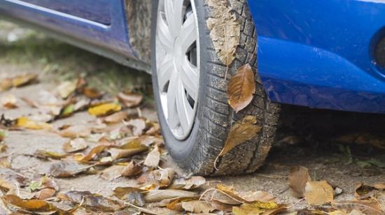 Nærbillede af hjulet i en blå bil parkeret på en vej fyldt med efterårsblade.