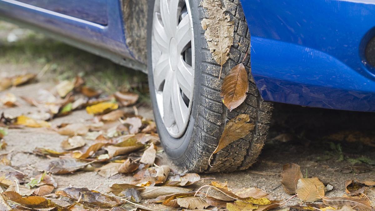 Nærbillede af hjulet i en blå bil parkeret på en vej fyldt med efterårsblade.