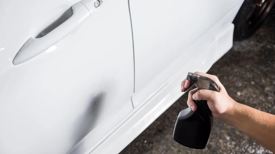 En person sprayer flyverustfjerner på siden av en hvit bil med mange små rustflekker.