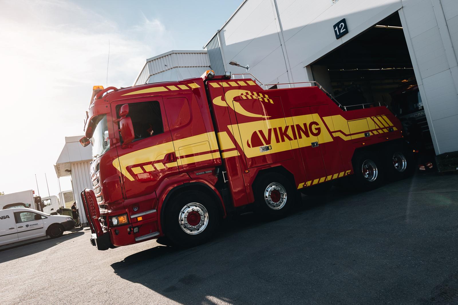 A red and yellow tow truck with the sign "Viking" drives out of the garage.