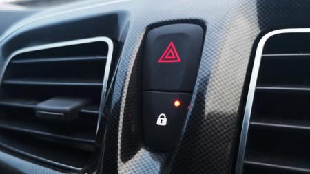 Auton kojelauta, jossa näkyy hätänappi punaisella kolmion symbolilla ja sen alla lukitusnappi punaisella varoitusvalolla.
