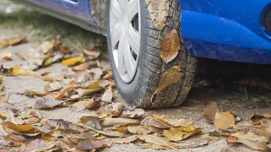 Närbild på hjulet av en blå bil parkerad på en väg fylld med höstlöv.