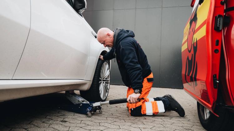 Viking tiepalvelun asiantuntija henkilö polvistuu ja nostaa tunkilla valkoista autoa.
