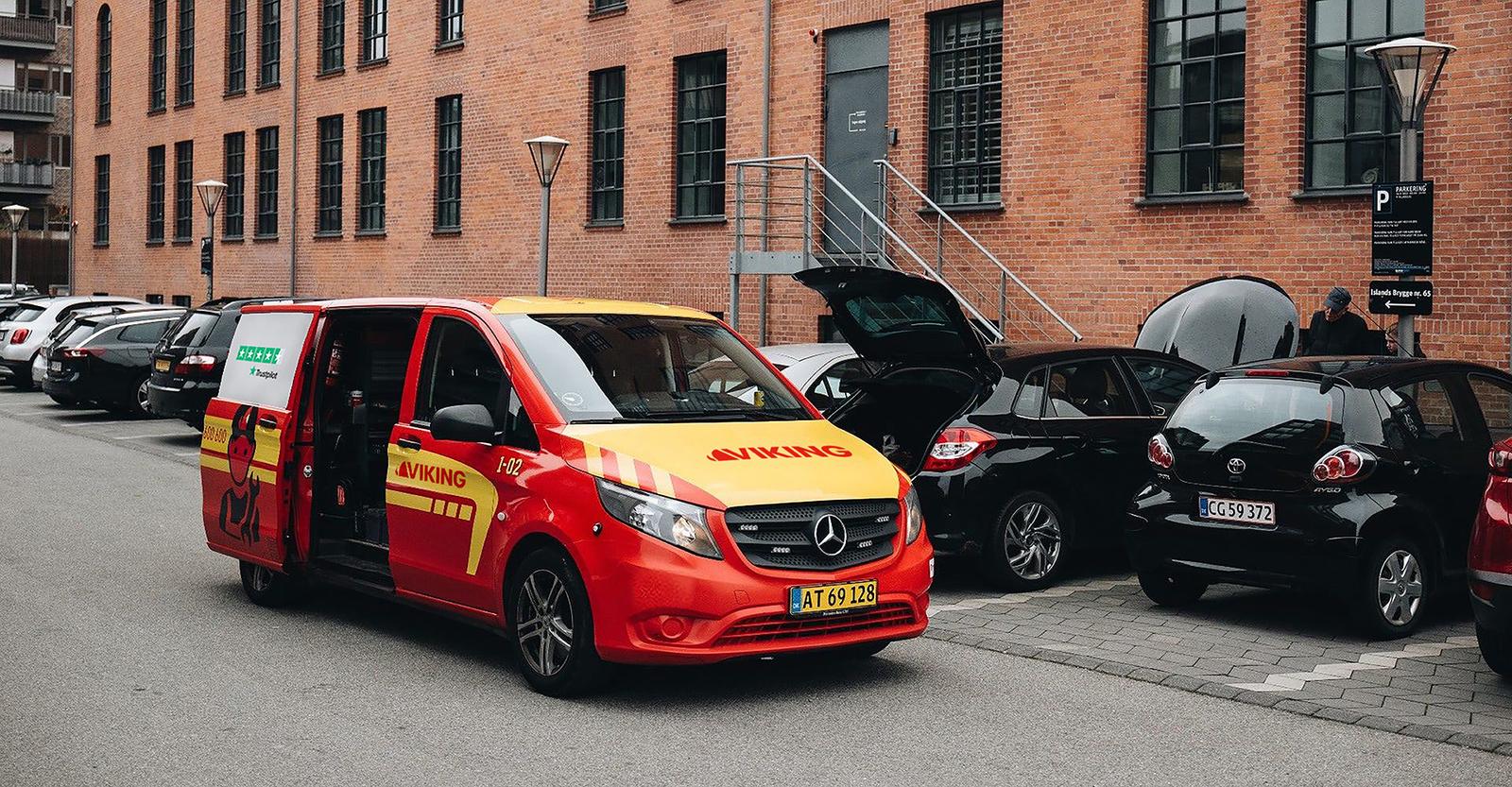 Punakeltainen Viking tiepalvelun pakettiauto on pysäköity kadulle autorivin viereen.