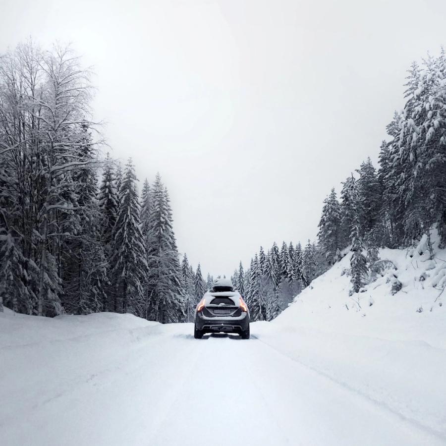 Auto ajaa lumista tietä pitkiä, jota ympäröi lumen peittämät puut.