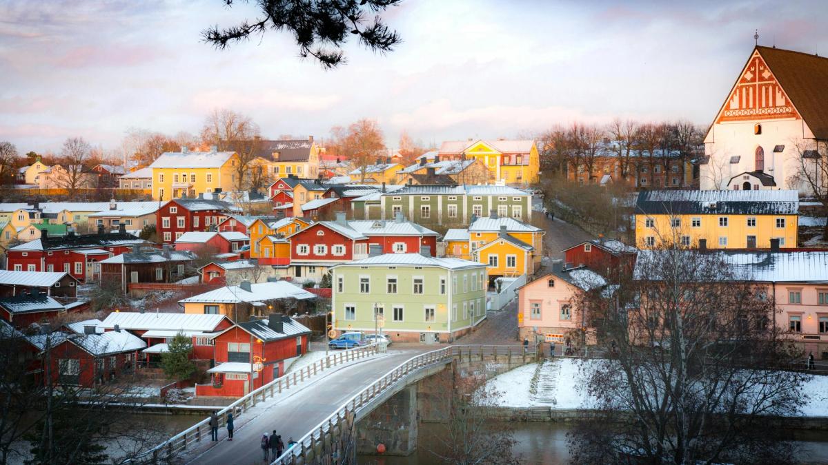 Porvoon jokirannan maisemaa, jossa on värikkäitä puutaloja, joen ylittävä silta ja suuri kirkko talvipäivänä.